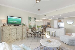 Uma sala de estar ampla com televisão, área de jantar, cozinha e um relógio na parede.
