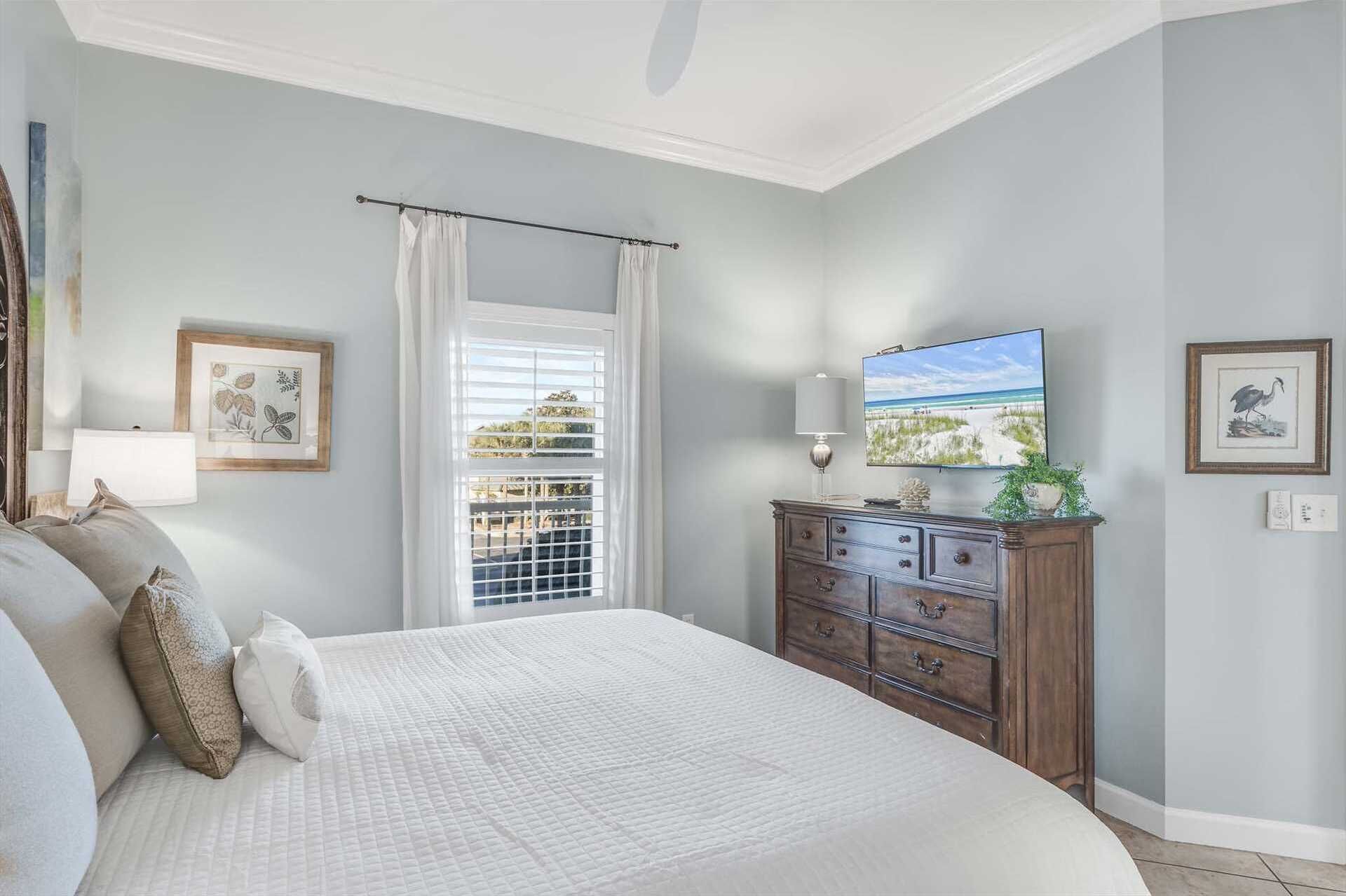A bedroom with a large bed, a dresser, a TV, and a window with curtains.