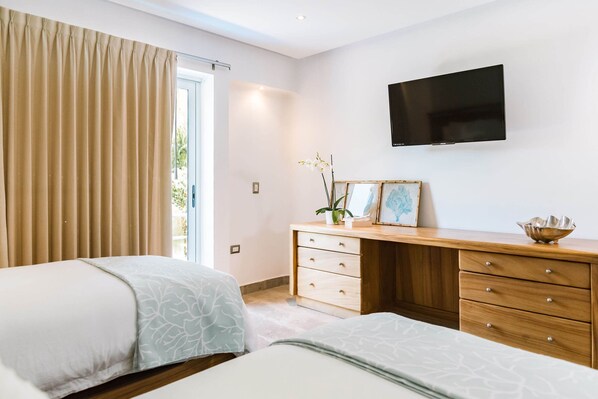 A hotel room with two beds, a wooden dresser, a flat-screen TV, and a sliding glass door to the outside.