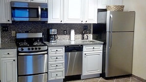 A compact kitchen with white cabinets, a stainless steel stove, a microwave, a dishwasher, and a refrigerator.