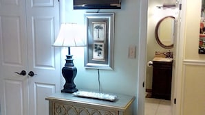 A bedroom with a bed, dresser, lamp, framed pictures, and a TV on the wall.