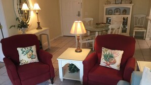 A living room with two red armchairs, a white coffee table, and a glass-top table with chairs. - St. Simons Island Beach Club Condo #126 (St. Simons Island)
