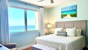 A bedroom with a bed, a ceiling fan, a painting of a beach, and a view of the ocean. - No Resort Fee~Gulf Front Double Balcony~Free Resort Chairs~Reserved Parking Spot (Panama City Beach)