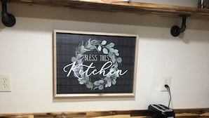 Una cucina con un piano di lavoro in legno, un cartello incorniciato con la scritta 'Bless This Kitchen' e un tostapane sul bancone.