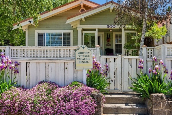 A picturesque entrance with blooming flowers, birch trees, and a copper roof.