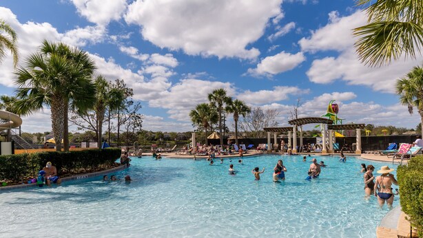 Una amplia piscina al aire libre rodeada de palmeras y sillones de descanso.