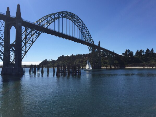 A large steel bridge spanning a body of water with a sailboat in the foreground. - Beverly beach delight (Newport)