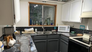 A modern kitchen with dark grey cabinets, a black marble countertop, a built-in oven, and a window with a view of trees. - Beverly beach delight (Newport)