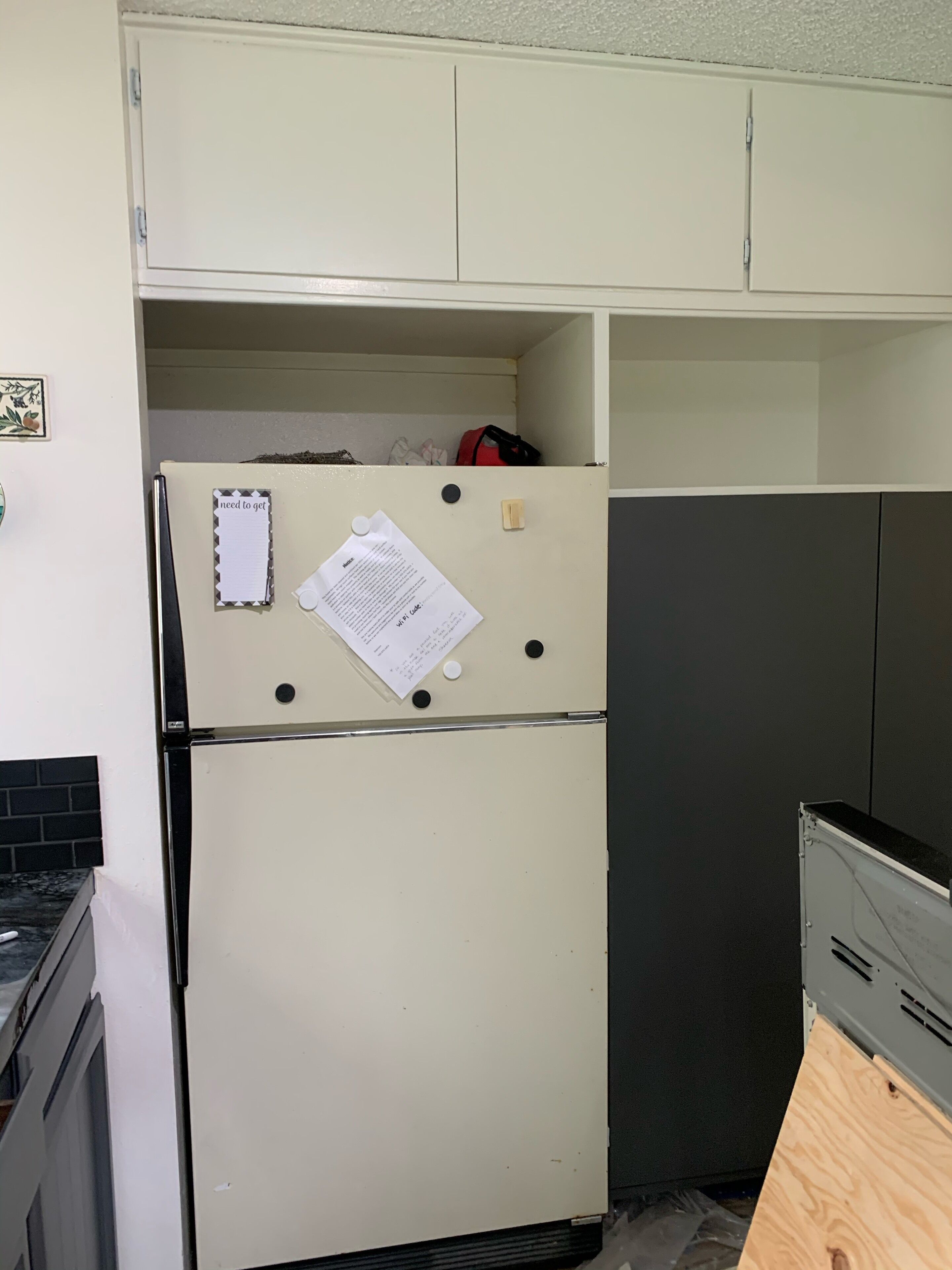 A compact kitchen with a white refrigerator, a wooden cabinet, and a black countertop.