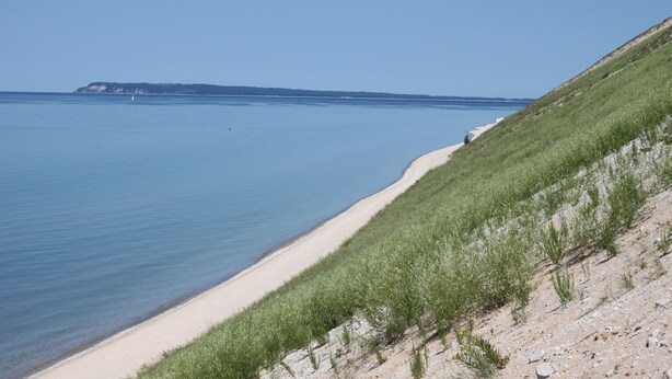 A coastal landscape with a sandy beach, grassy dunes, and a calm sea. - Long Lake Waterfront Cottage (Traverse City)