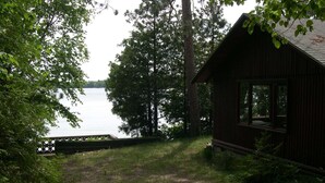 A cabin by a lake with a wooden deck and a grassy path leading to it. - Long Lake Waterfront Cottage (Traverse City)
