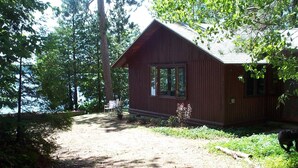 A cabin with a large window, surrounded by trees and a dirt path. - Long Lake Waterfront Cottage (Traverse City)