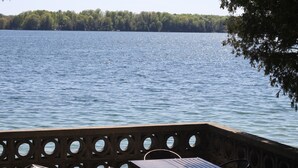 A lakeside view with a table and chairs, a metal railing, and a bag on the ground. - Long Lake Waterfront Cottage (Traverse City)