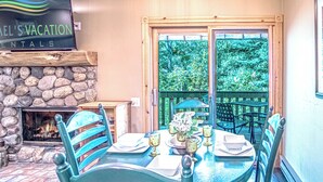 A dining area with a stone fireplace, a table set for four, and a view of the outdoors through a glass door. - SV113 - Walk to Lifts & Town - Hot Tub & Pool (Ketchum)