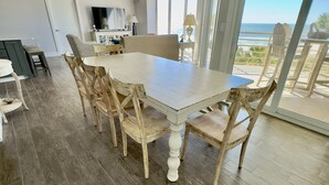A spacious dining area with a white table and wooden chairs, a ceiling fan, and a view of the ocean through large sliding doors. - Spacious Oceanfront Condo in Palmetto Dunes, Unobstructed Ocean Views  (Hilton Head Island)