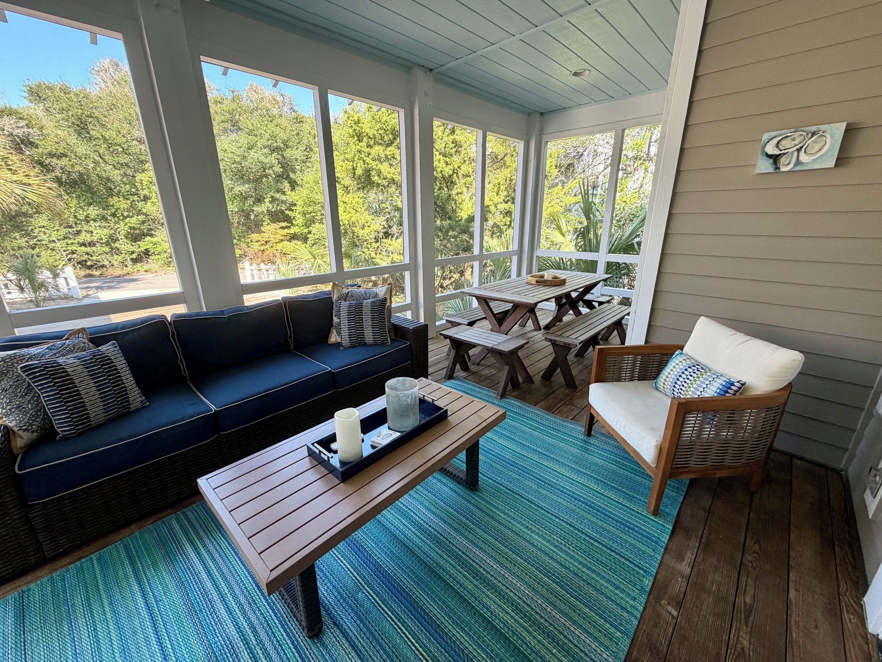 A covered porch with a dark blue sofa, a wooden table, and a wicker chair.