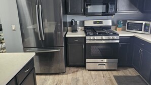 Cozinha moderna com eletrodomésticos de aço inoxidável, armários escuros e micro-ondas.