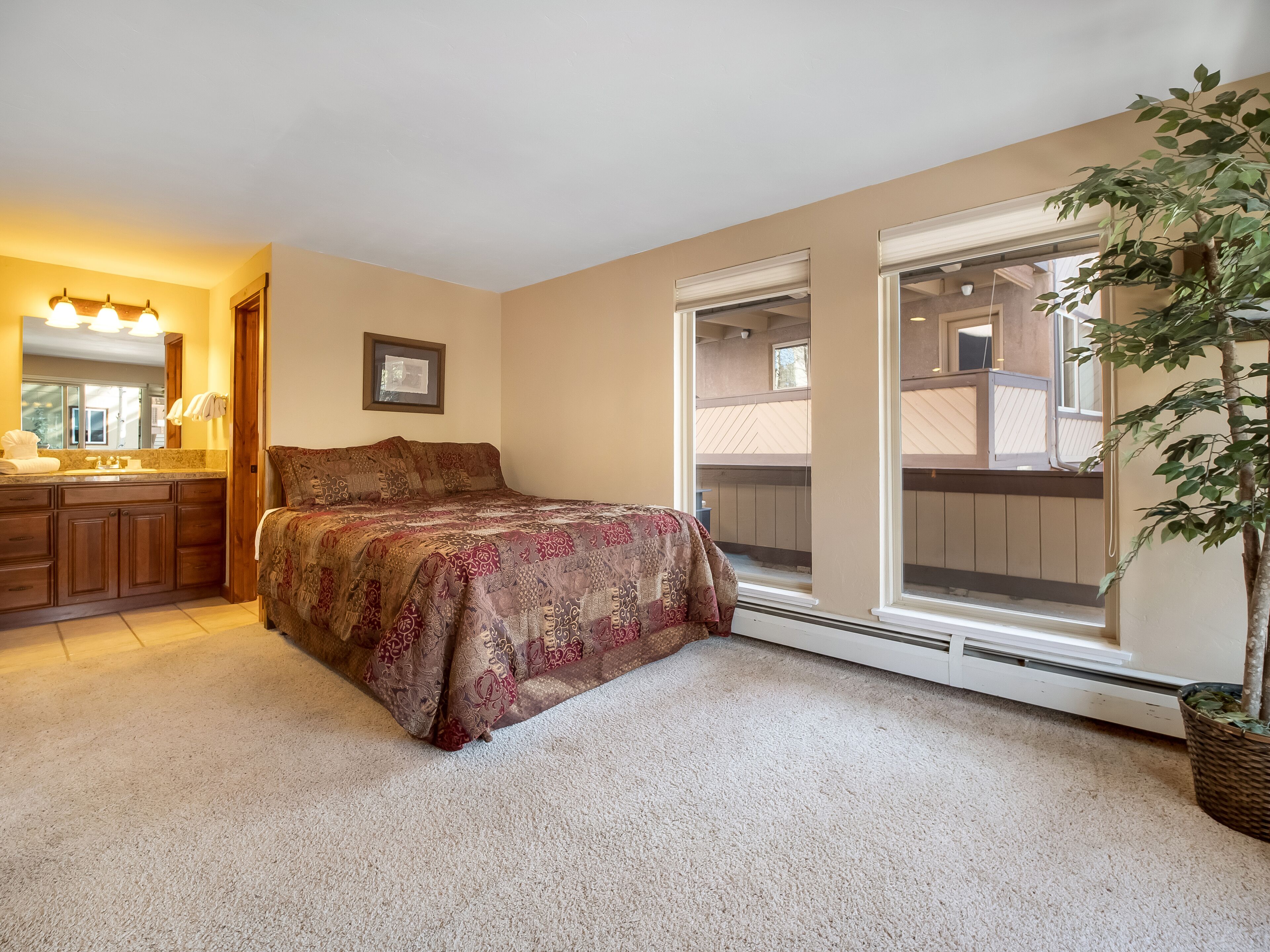 A bedroom with a large bed, a bathroom with a vanity, and a sliding glass door to a balcony.