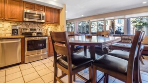 A modern kitchen with wooden cabinets, stainless steel appliances, and a large dining table with chairs. - Cozy unit walking distance to Quick Silver Ski Lift and free parking. (Breckenridge)