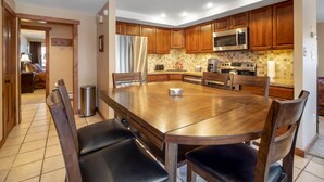 A modern kitchen with wooden cabinets, stainless steel appliances, and a large dining table with chairs. - Cozy unit walking distance to Quick Silver Ski Lift and free parking. (Breckenridge)