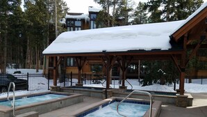 A pool area with three hot tubs, surrounded by a wooden gazebo, set against a backdrop of snow-covered trees and buildings. - Cozy unit walking distance to Quick Silver Ski Lift and free parking. (Breckenridge)