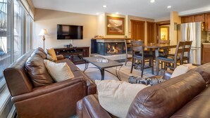 A modern living room with a fireplace, leather sofas, a flat-screen TV, and a dining area with wooden chairs. - Cozy unit walking distance to Quick Silver Ski Lift and free parking. (Breckenridge)