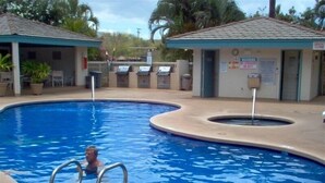 Una piscina con una silla de salvavidas y un socorrista. Hay sillas de descanso y un pequeño edificio con un letrero.