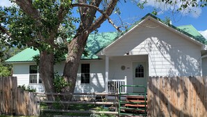 Un bâtiment blanc surmonté d’un toit vert, avec une clôture en bois et un chemin de gravier menant à l’entrée.