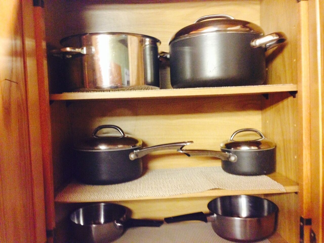 A kitchen cabinet with stainless steel pots and pans organized on shelves.