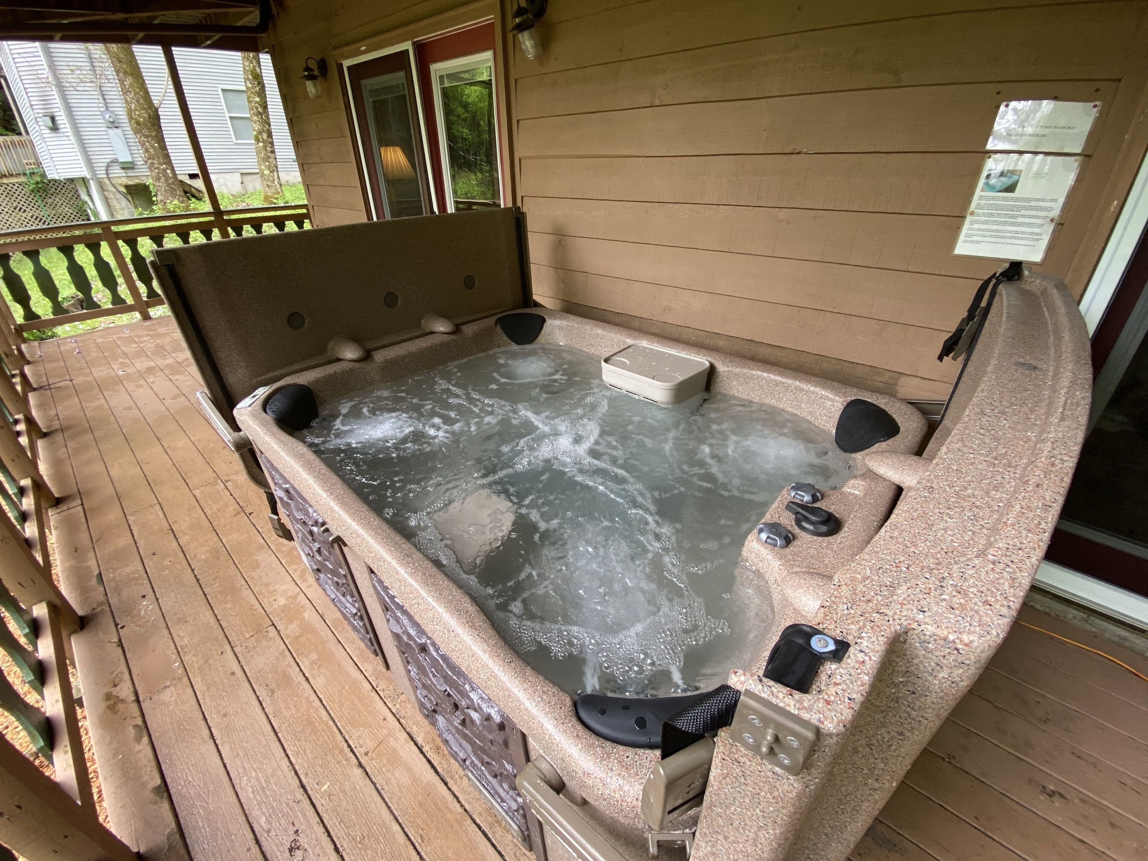 A hot tub on a wooden deck with a view of a house in the background.