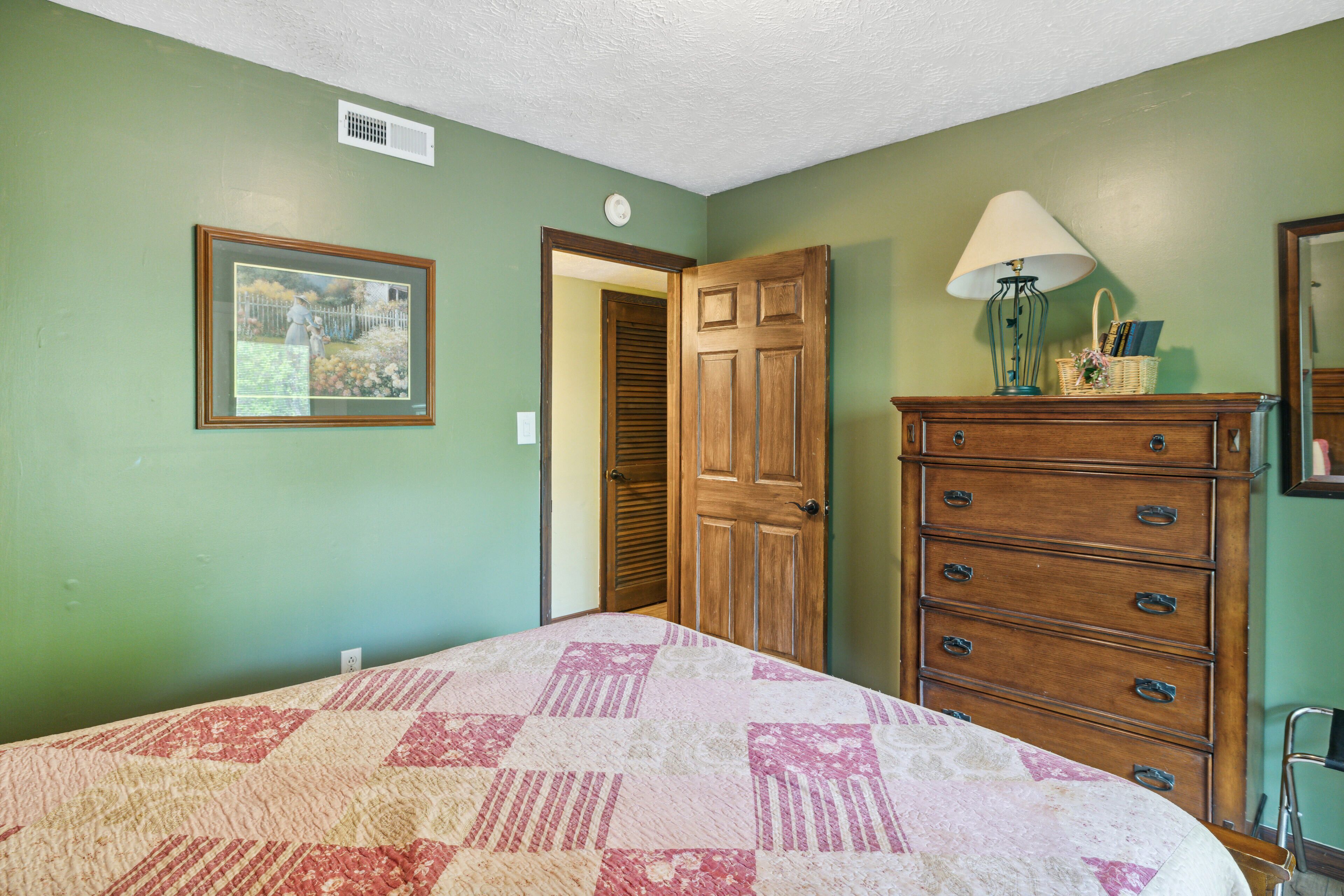 A bedroom with a bed, a dresser, a lamp, and a framed picture on the wall.