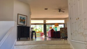 Un escalier menant à un espace de vie comprenant un ventilateur de plafond, un canapé et un fauteuil.