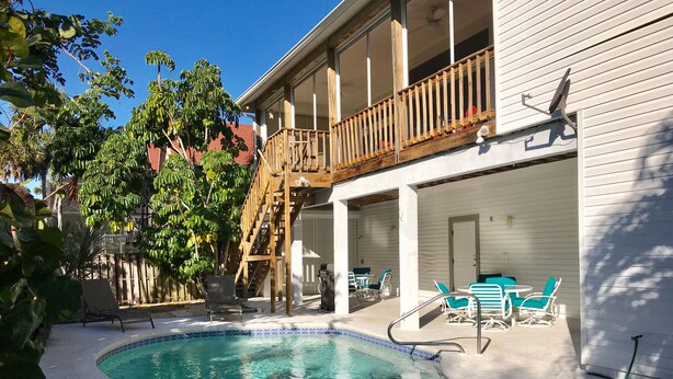 Un espace piscine doté d’une terrasse en bois, de sièges extérieurs et d’un escalier menant à un balcon.