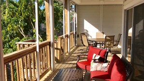 Un espace extérieur abrité, aménagé avec du mobilier en bois, notamment un canapé rouge et une table, et doté d’un ventilateur de plafond.