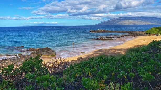 Una spiaggia con cielo sereno, costa rocciosa e montagne all'orizzonte.
