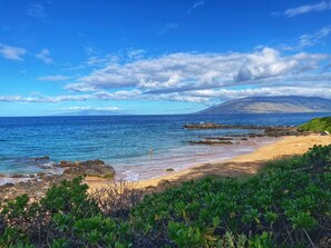 A beach with clear blue water, rocky shore, and a mountain in the background. - Guests Love Our Condo. You Will Too! (Kihei)