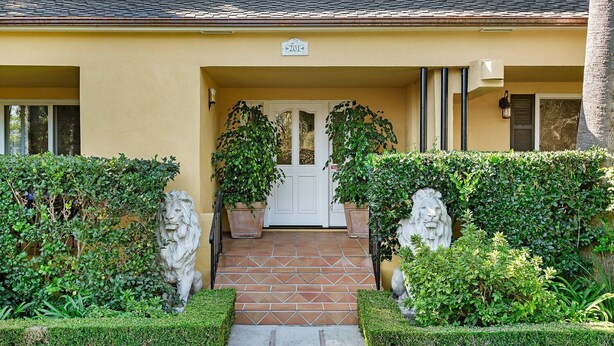 A building entrance with a tiled pathway leading to a white door, flanked by two stone lion statues and potted plants. - Rare Beach Penthouse — blocks to the Beach and Funk Zone (Santa Barbara)