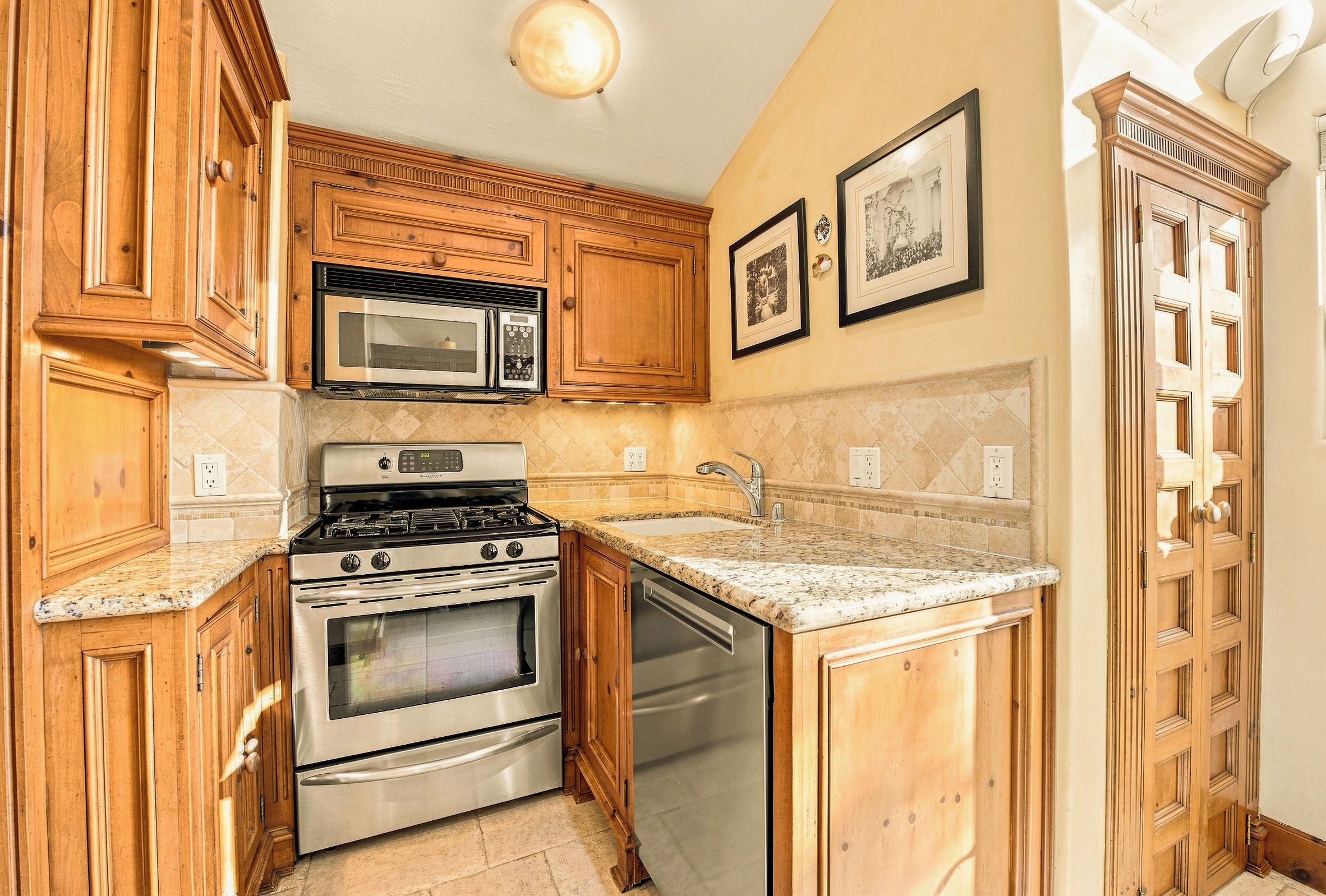 A kitchen with wooden cabinets, stainless steel appliances, a granite countertop, and a wall-mounted light fixture.