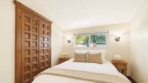 A bedroom with a large wooden wardrobe, a bed with white bedding, two bedside tables with lamps, and a window with a view of greenery. - Rare Beach Penthouse — blocks to the Beach and Funk Zone (Santa Barbara)