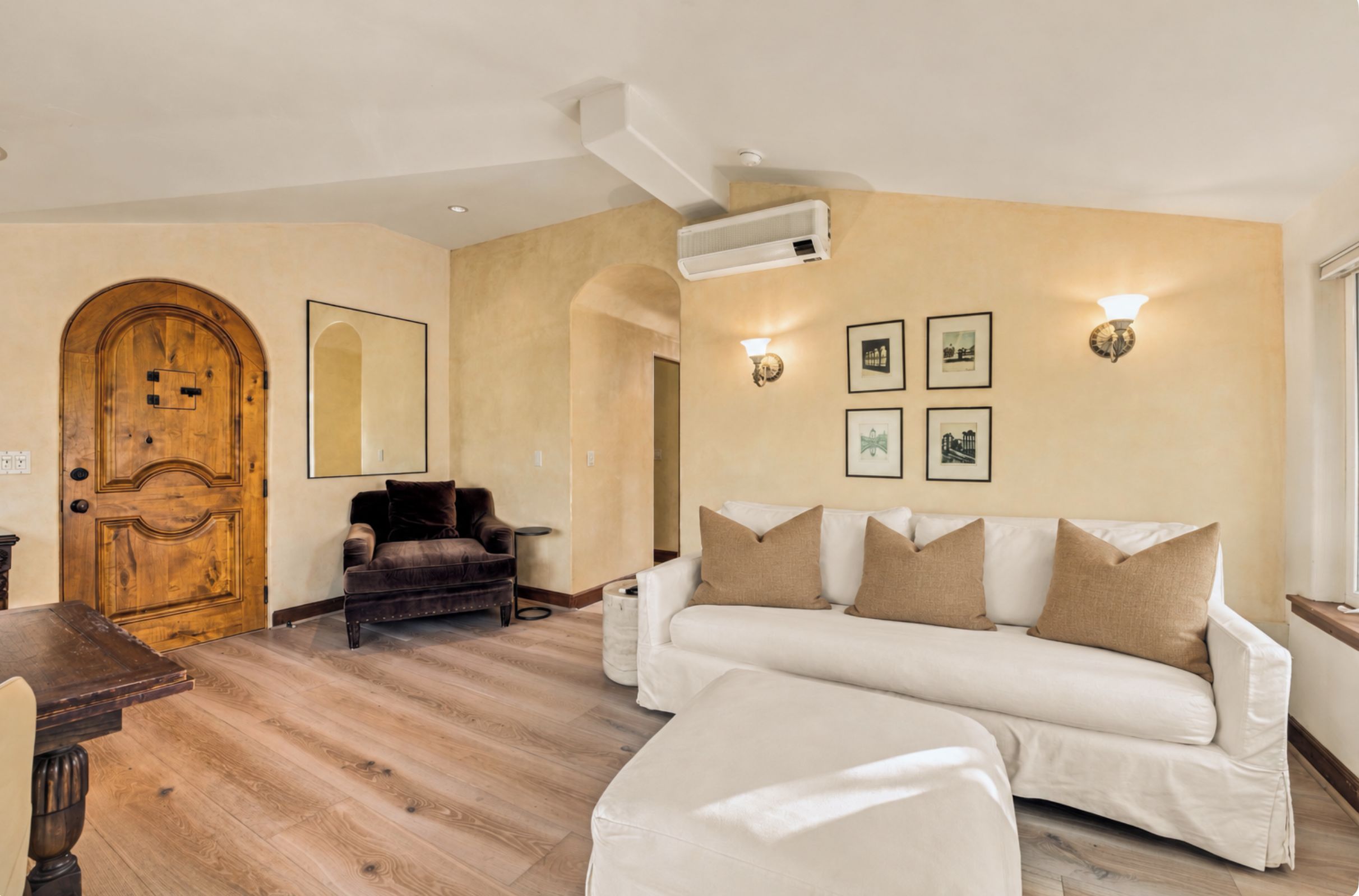 Ein Wohnzimmer mit einer Holztür, einem braunen Ledersofa, einem weißen Sofa und einem Holztisch.