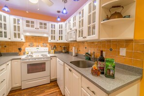 A kitchen with white cabinets, a stove, and a sink. There are bottles and a bag on the counter.