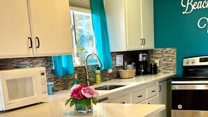 A modern kitchen with a central island, white cabinetry, a stainless steel oven, and a teal accent wall. - Romantic Riverfront Retreat with Covered Deck & Fire Pit-walk to Beach! (Seaside)
