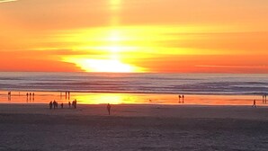 A beach at sunset with people walking along the shore. - Romantic Riverfront Retreat with Covered Deck & Fire Pit-walk to Beach! (Seaside)