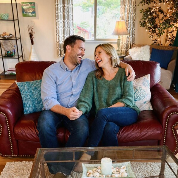 A couple sitting on a red leather couch with a glass coffee table in front of them.