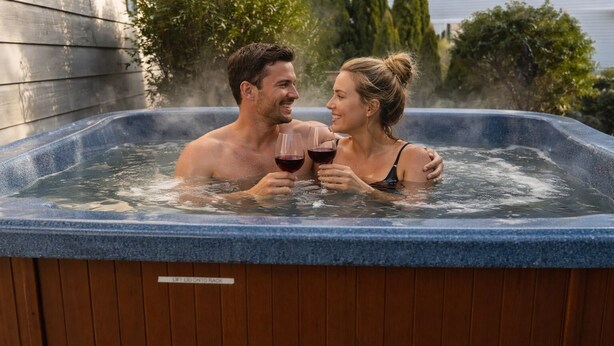 A couple in a hot tub with a wooden exterior and a label indicating it can be lifted onto a rack. - Romantic Riverfront Retreat with Covered Deck & Fire Pit-walk to Beach! (Seaside)