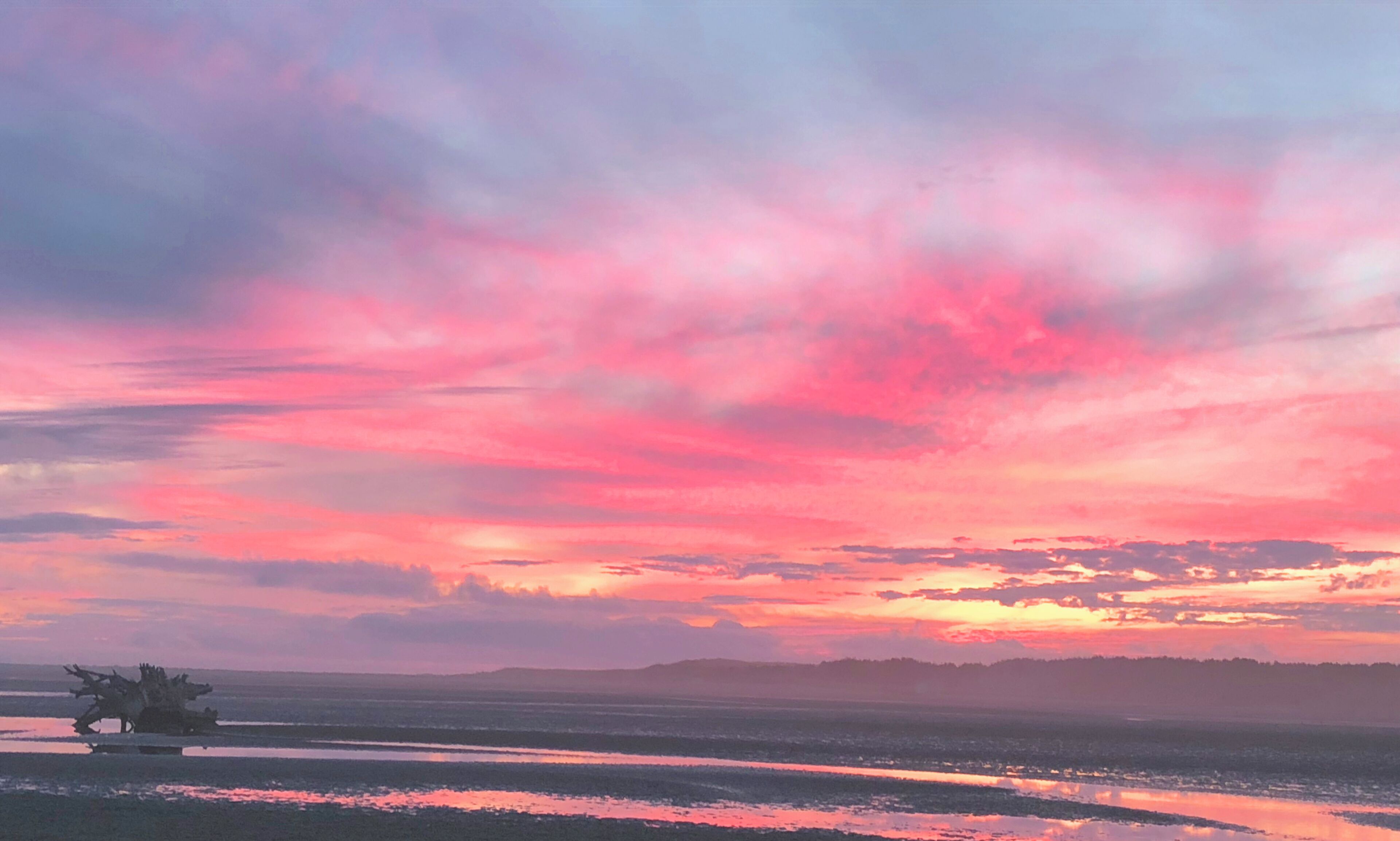 A sunset over a flat landscape with a body of water reflecting the sky.