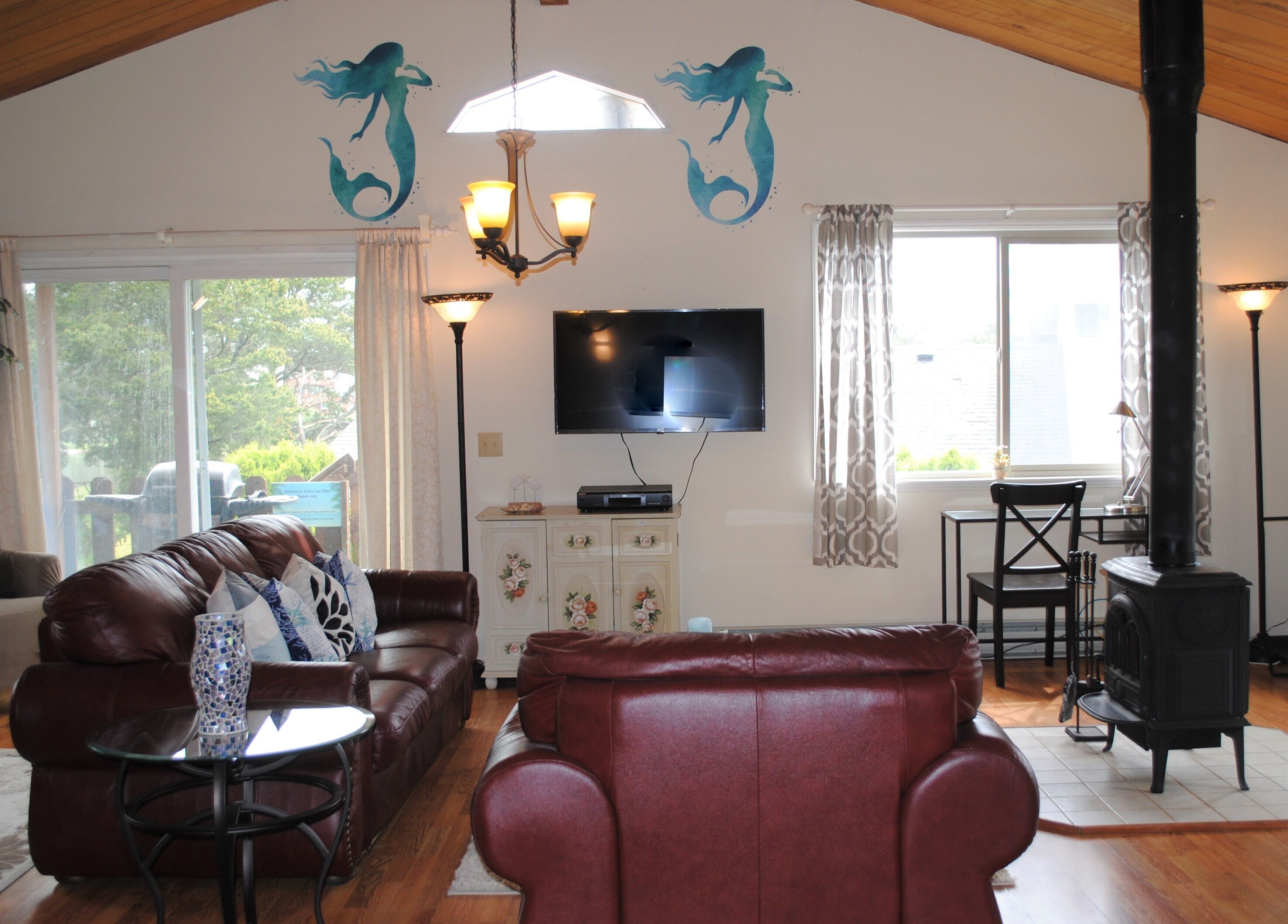 A living room with a brown leather sofa, a red armchair, a glass coffee table, a fireplace, and a television mounted on the wall.