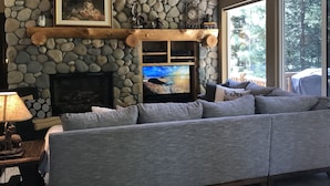Ein gemütliches Wohnzimmer mit Kamin aus Stein, einem Fernseher und einem grauen Sofa.