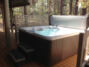 Relax in the hot tub on the outdoor deck, surrounded by a forest.