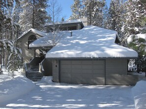 A two-story house with a garage, surrounded by snow-covered trees.